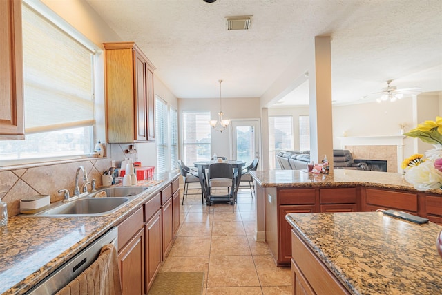 kitchen featuring dishwasher, sink, backsplash, a tiled fireplace, and ceiling fan with notable chandelier