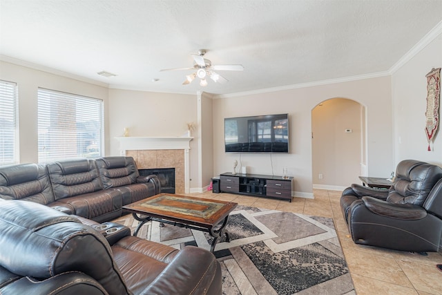 living room with ceiling fan, light tile patterned floors, crown molding, and a tile fireplace