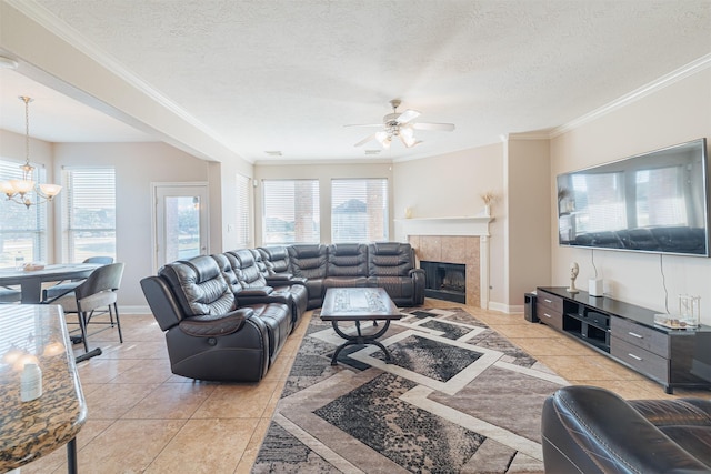 living room featuring ceiling fan with notable chandelier, light tile patterned floors, a fireplace, ornamental molding, and a textured ceiling