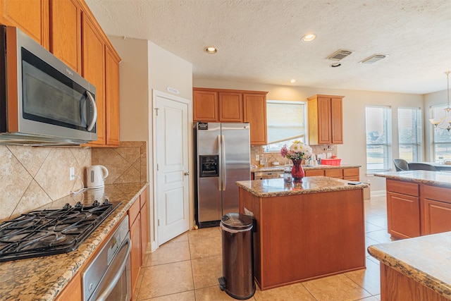 kitchen featuring a kitchen island, light tile patterned flooring, stainless steel appliances, and an inviting chandelier