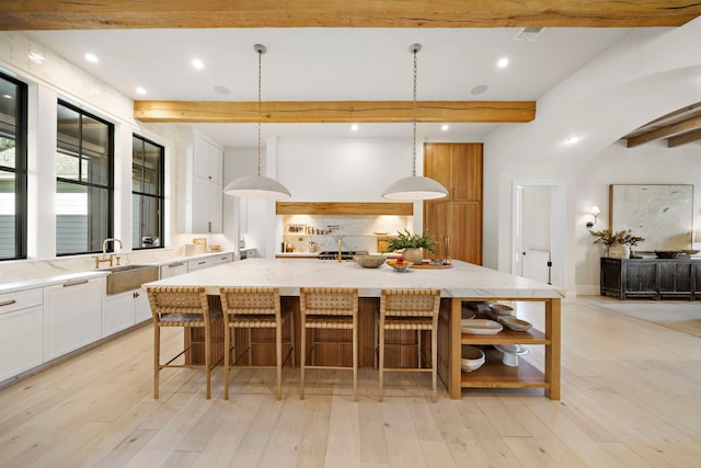 kitchen featuring white cabinetry, a large island, sink, beam ceiling, and pendant lighting