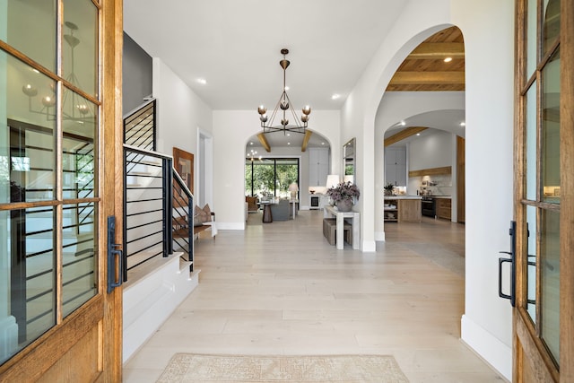 foyer entrance featuring a notable chandelier, beamed ceiling, and light hardwood / wood-style floors