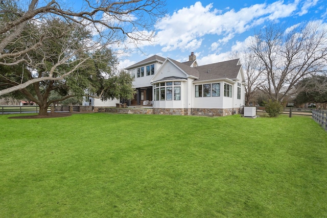 rear view of house featuring central AC unit and a lawn