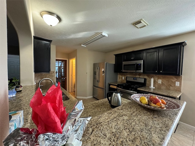 kitchen with sink, decorative backsplash, a textured ceiling, kitchen peninsula, and stainless steel appliances