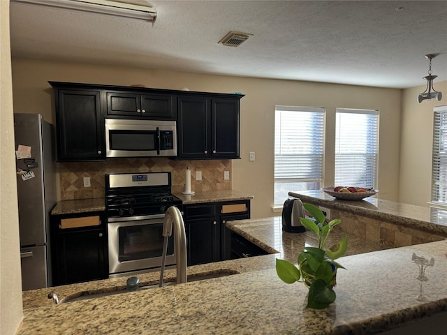 kitchen with a textured ceiling, light stone countertops, backsplash, and appliances with stainless steel finishes