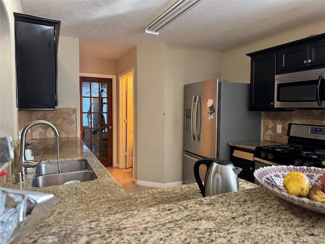 kitchen with sink, a textured ceiling, appliances with stainless steel finishes, tasteful backsplash, and light stone counters