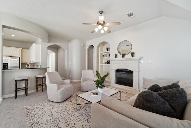 living room featuring sink, vaulted ceiling, ceiling fan, built in features, and light colored carpet