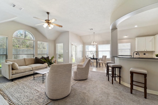 carpeted living room with lofted ceiling, sink, a textured ceiling, and ceiling fan with notable chandelier