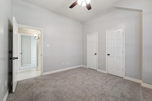 unfurnished bedroom featuring ceiling fan, vaulted ceiling, light carpet, and multiple closets