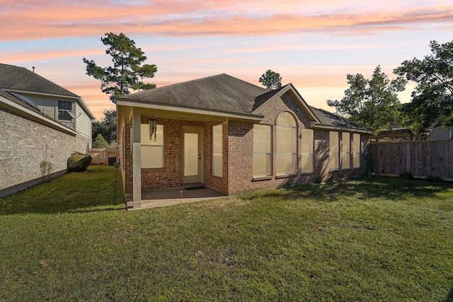 back house at dusk featuring a lawn and a patio area