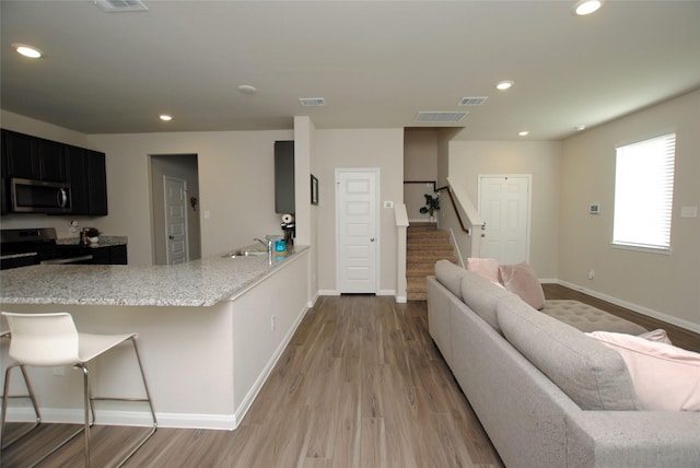 kitchen featuring black electric range oven, a kitchen breakfast bar, sink, light stone countertops, and light hardwood / wood-style floors