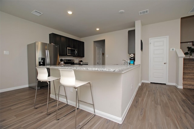 kitchen featuring stainless steel appliances, light stone counters, kitchen peninsula, a breakfast bar, and light wood-type flooring