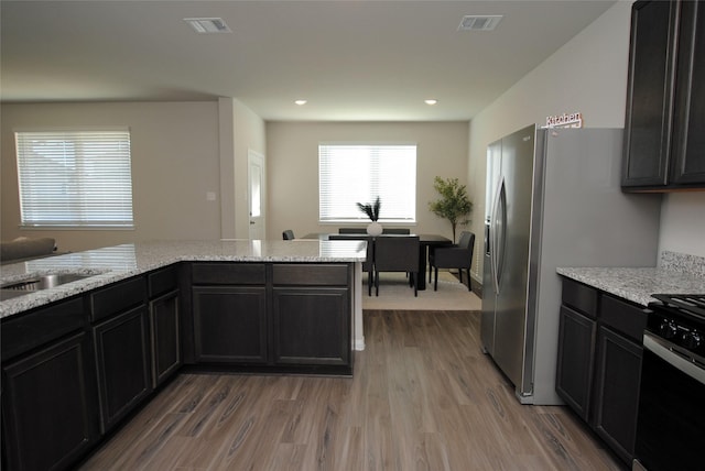 kitchen featuring stove, hardwood / wood-style flooring, light stone counters, and sink