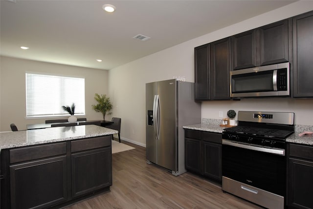 kitchen with dark brown cabinets, light stone counters, wood-type flooring, and stainless steel appliances