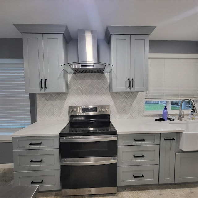 kitchen featuring stainless steel electric range oven, sink, wall chimney exhaust hood, backsplash, and gray cabinets