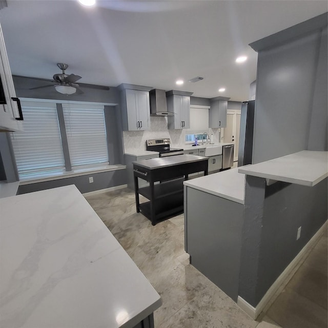 kitchen with backsplash, wall chimney range hood, ceiling fan, gray cabinets, and appliances with stainless steel finishes