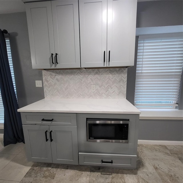 kitchen featuring decorative backsplash, light stone counters, and gray cabinetry