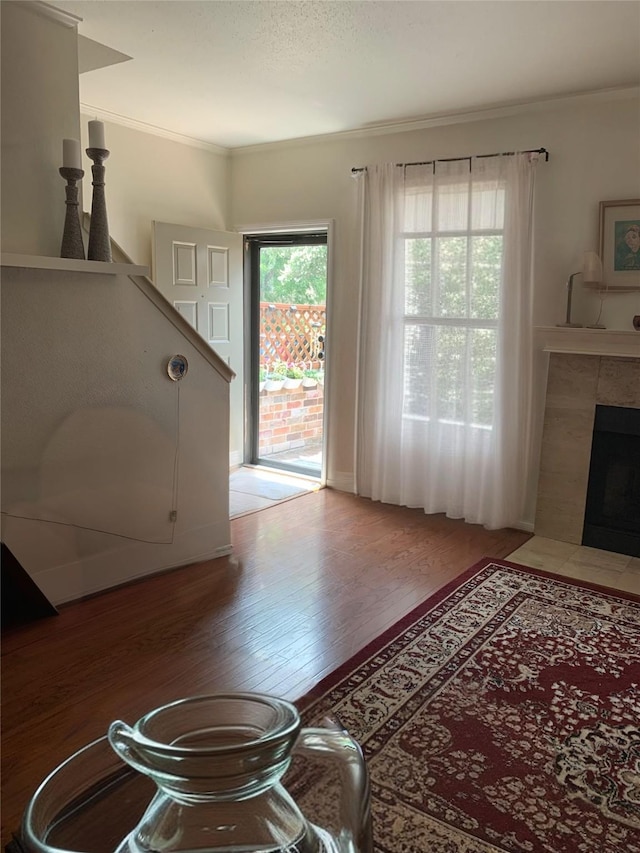 interior space featuring a tile fireplace, hardwood / wood-style flooring, a wealth of natural light, and crown molding