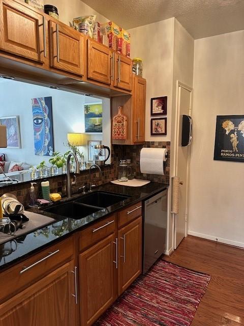 kitchen featuring sink, dark wood-type flooring, stainless steel dishwasher, dark stone countertops, and a textured ceiling