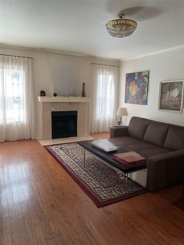 living room with ornamental molding, a textured ceiling, ceiling fan, hardwood / wood-style flooring, and a tiled fireplace