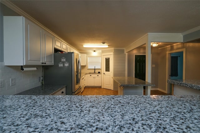 kitchen featuring kitchen peninsula, tasteful backsplash, dark stone counters, white cabinets, and stainless steel refrigerator