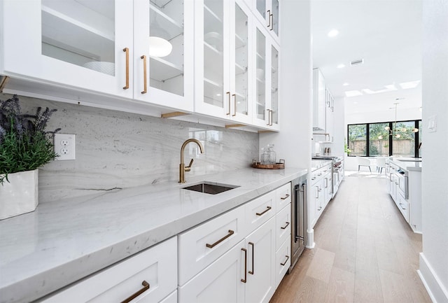 kitchen featuring decorative backsplash, light stone counters, white cabinetry, and sink