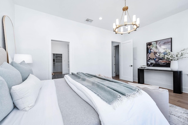 bedroom with wood-type flooring, a walk in closet, and a notable chandelier