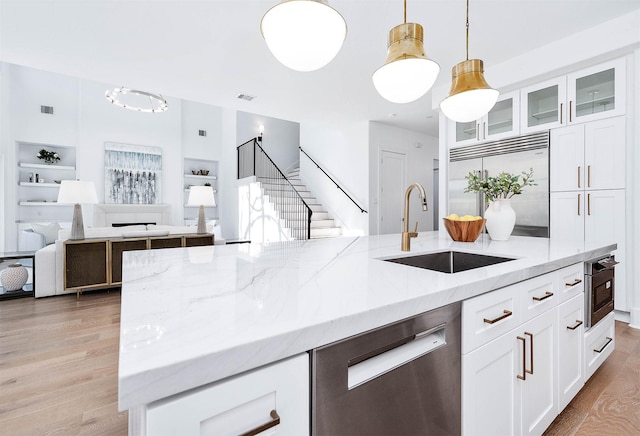 kitchen featuring light stone countertops, stainless steel appliances, sink, decorative light fixtures, and white cabinetry