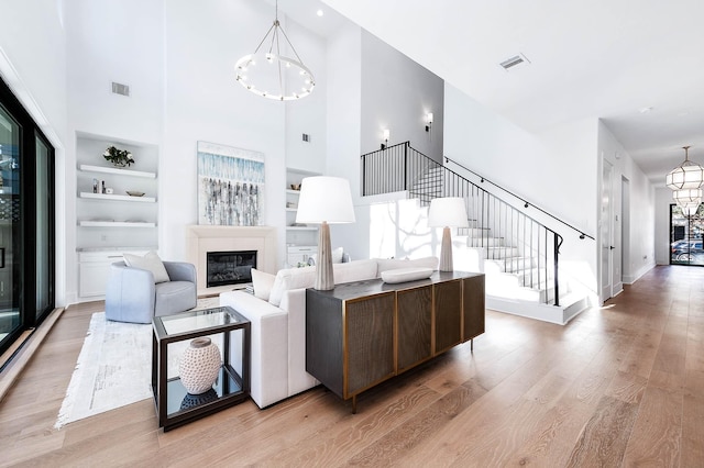 living room featuring a notable chandelier, light wood-type flooring, a towering ceiling, and built in shelves