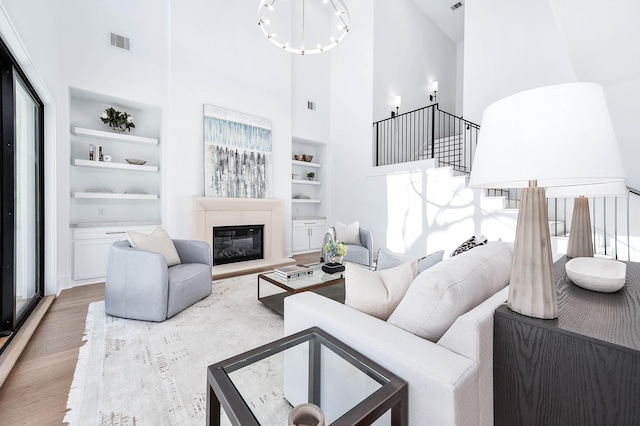 living room with built in shelves, a towering ceiling, and light hardwood / wood-style flooring