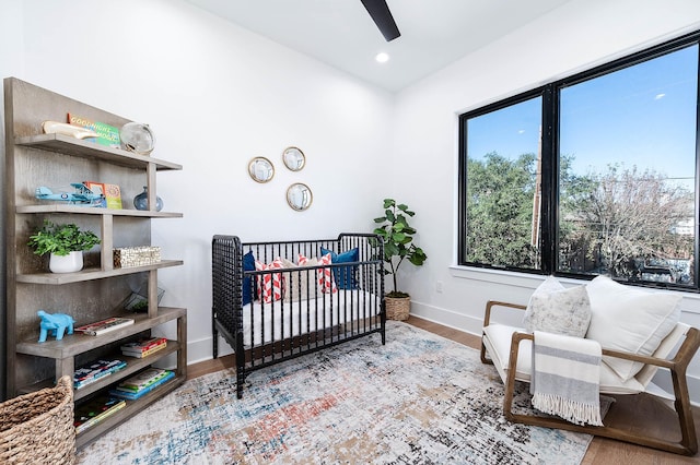 bedroom with a crib, wood-type flooring, and ceiling fan