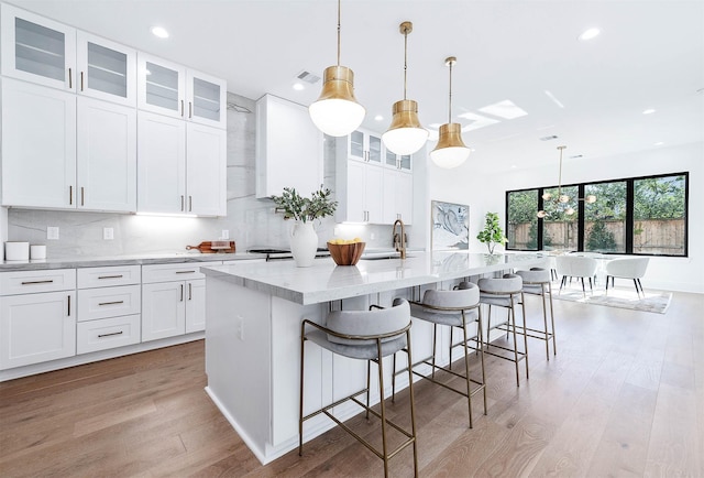 kitchen with white cabinetry, hanging light fixtures, and an island with sink