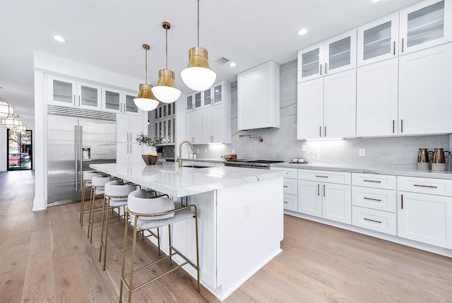 kitchen featuring stainless steel built in refrigerator, decorative light fixtures, white cabinets, and a kitchen island with sink