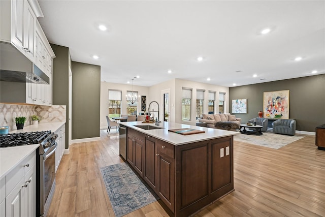 kitchen featuring appliances with stainless steel finishes, dark brown cabinets, a kitchen island with sink, sink, and light hardwood / wood-style flooring