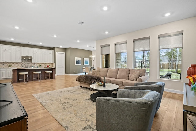 living room featuring light wood-type flooring, sink, and a chandelier