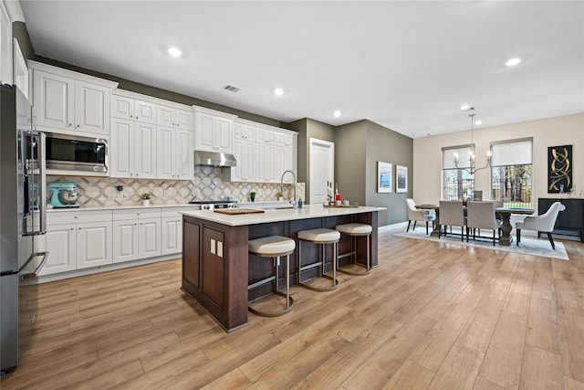 kitchen featuring a center island with sink, decorative light fixtures, white cabinetry, stainless steel appliances, and a chandelier