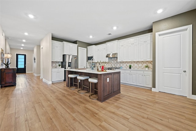 kitchen with light wood-type flooring, backsplash, a breakfast bar, a kitchen island with sink, and white cabinetry