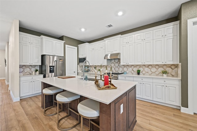 kitchen featuring a center island with sink, white cabinets, a breakfast bar area, and stainless steel appliances