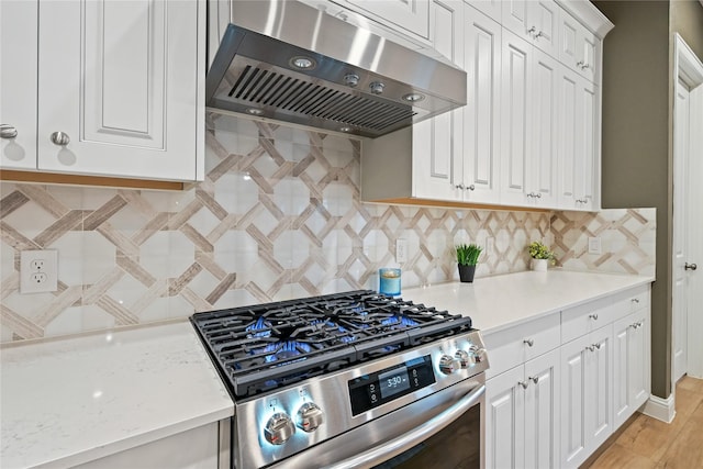 kitchen featuring decorative backsplash, light stone counters, stainless steel range, exhaust hood, and white cabinetry