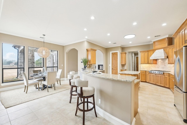 kitchen featuring premium range hood, appliances with stainless steel finishes, decorative backsplash, hanging light fixtures, and light stone countertops