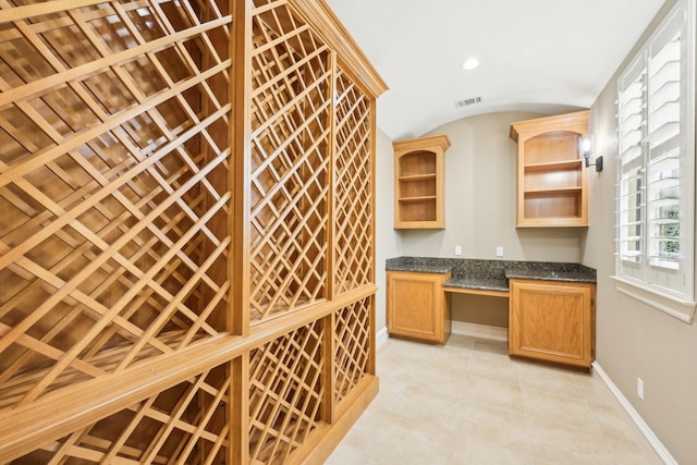 wine area with light tile patterned flooring, built in desk, and vaulted ceiling