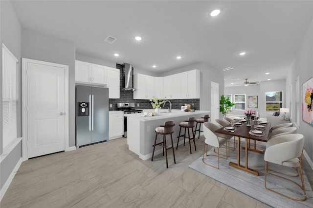 kitchen featuring kitchen peninsula, appliances with stainless steel finishes, a kitchen breakfast bar, wall chimney range hood, and white cabinets