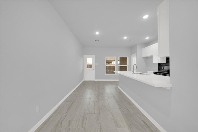 kitchen with stove, backsplash, white cabinets, sink, and kitchen peninsula