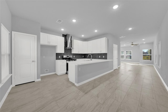 kitchen with wall chimney range hood, sink, ceiling fan, stainless steel range, and white cabinetry