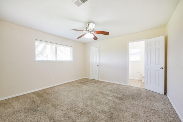 unfurnished bedroom with multiple windows, light colored carpet, ceiling fan, and ensuite bathroom