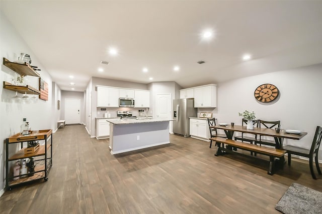 kitchen with appliances with stainless steel finishes, light stone counters, a kitchen island with sink, dark wood-type flooring, and white cabinets