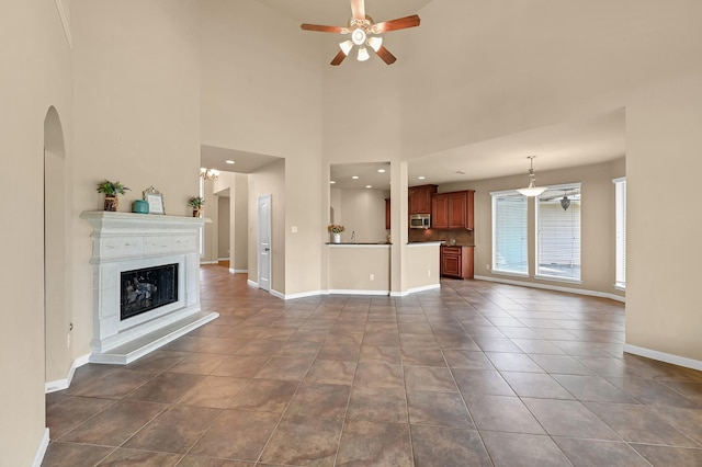 unfurnished living room featuring ceiling fan with notable chandelier, dark tile patterned floors, and a towering ceiling