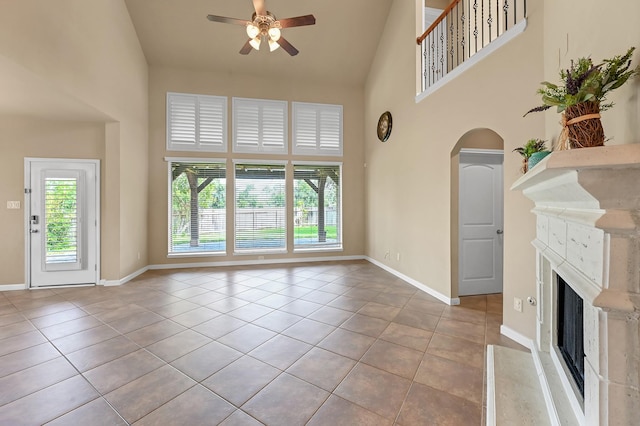 unfurnished living room featuring ceiling fan, a towering ceiling, a high end fireplace, and light tile patterned floors