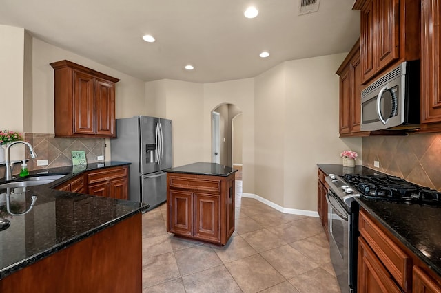 kitchen with sink, dark stone countertops, light tile patterned floors, a kitchen island, and stainless steel appliances