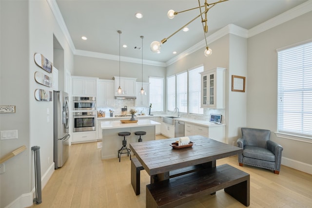 kitchen featuring crown molding, appliances with stainless steel finishes, white cabinetry, hanging light fixtures, and a center island